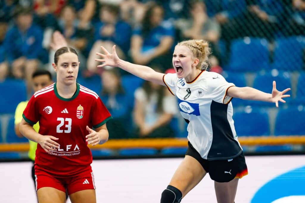 A player in a white and black uniform celebrates enthusiastically on the court while an opponent in a red jersey watches.